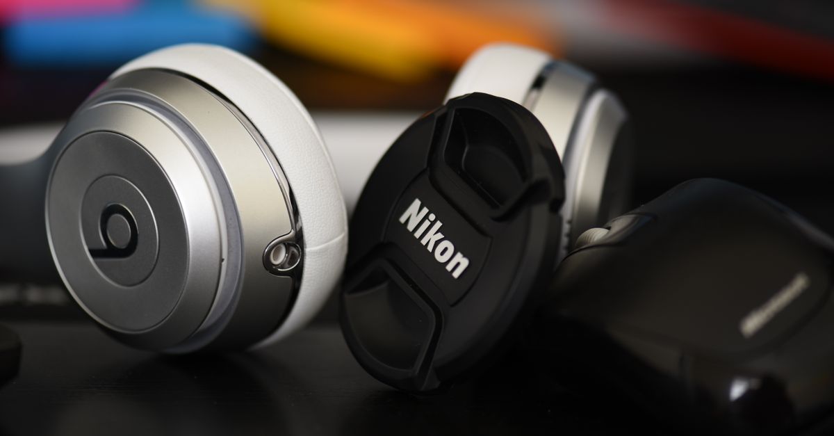 Detailed close-up of silver headphones and a Nikon lens cap on a dark surface.